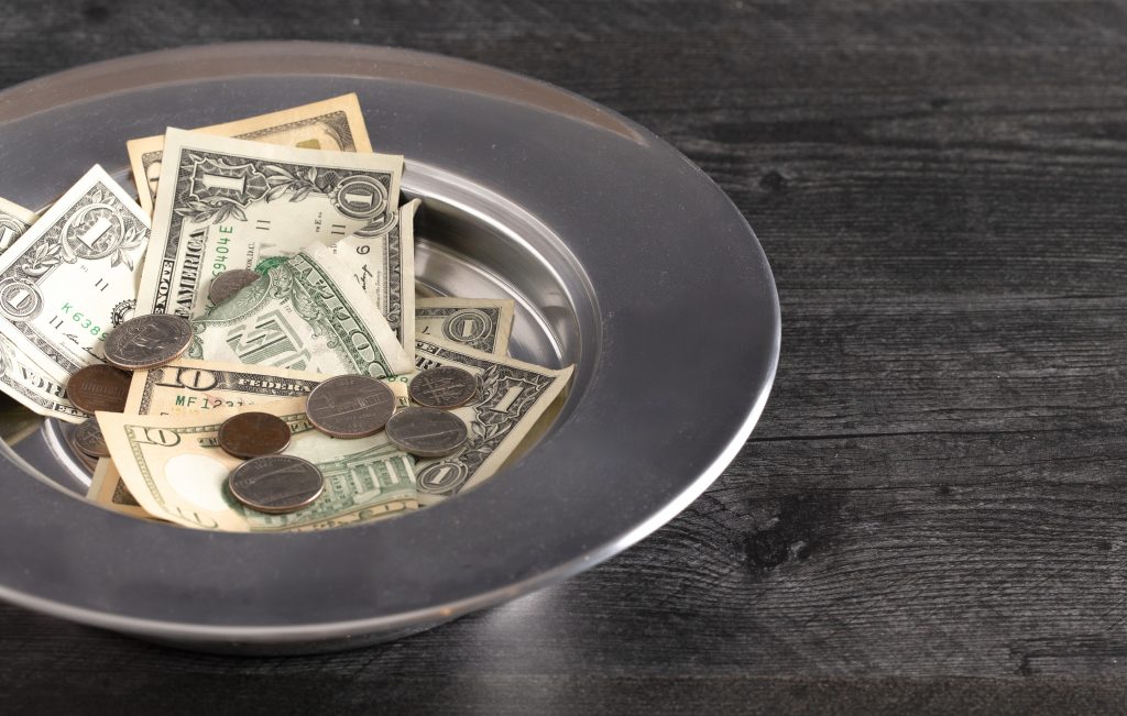 A silver collection plate filled with cash donations for a faith-based organization.