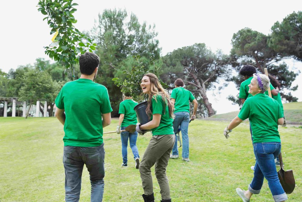 Group of volunteers walking in a field with shovels, wheelbarrows, and two small trees to plant for major donor gift ideas